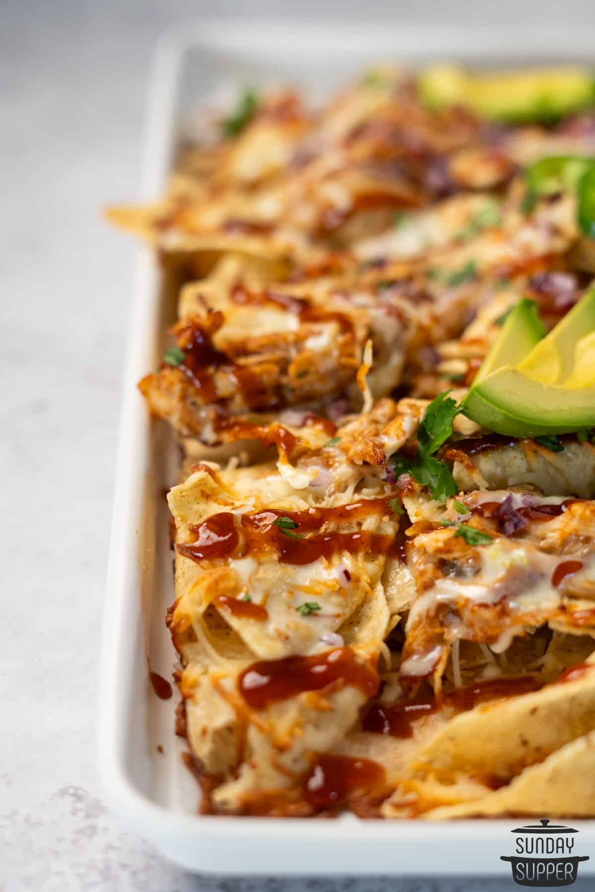 chicken nachos on a baking tray with cilantro and avocado