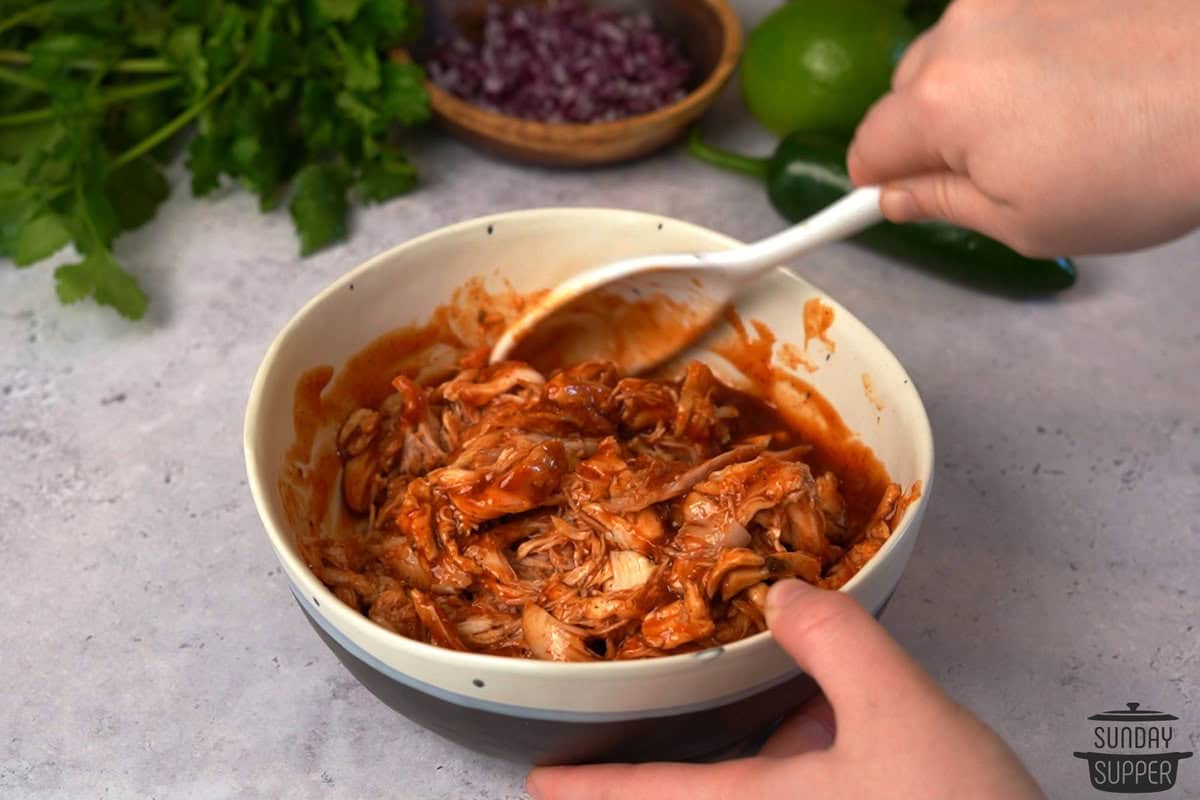 sauce being stirred into the shredded chicken