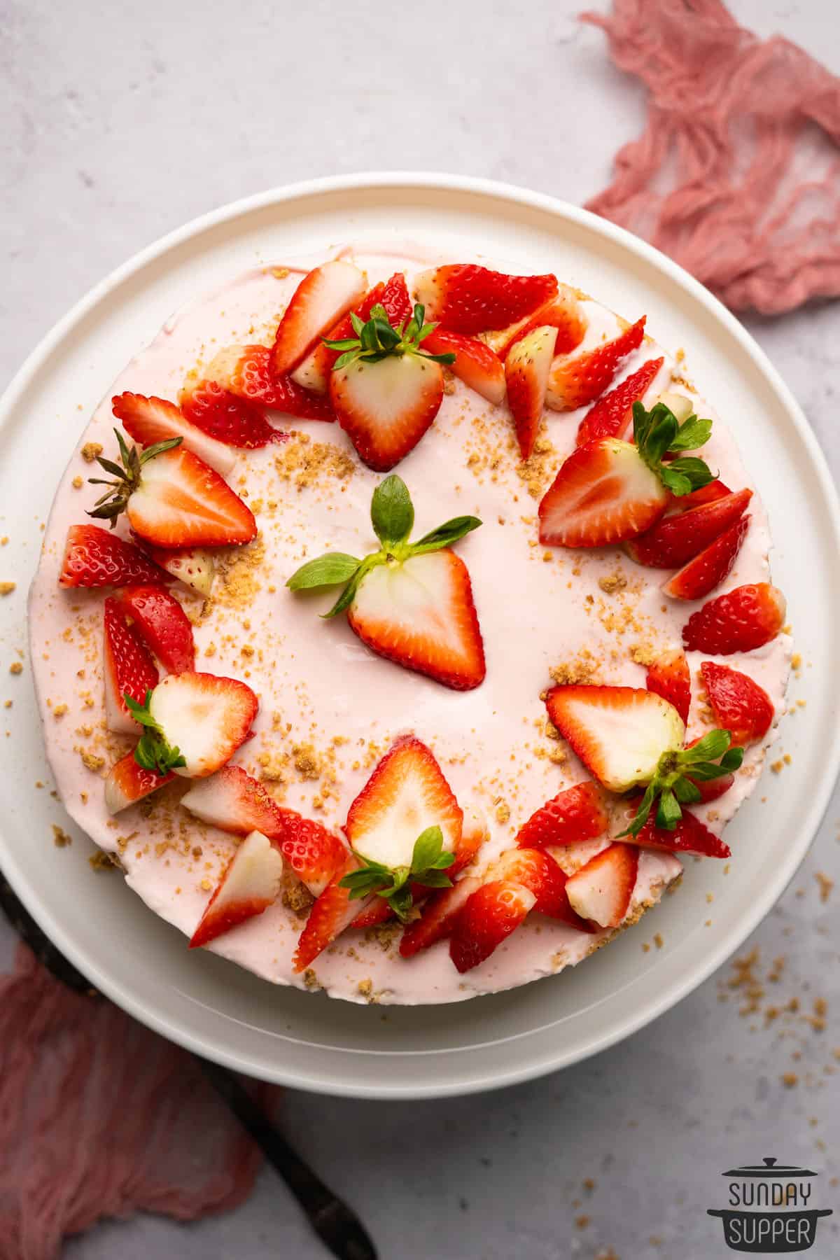 a top down view of a strawberry cheesecake on a serving plate decorated with fresh strawberries