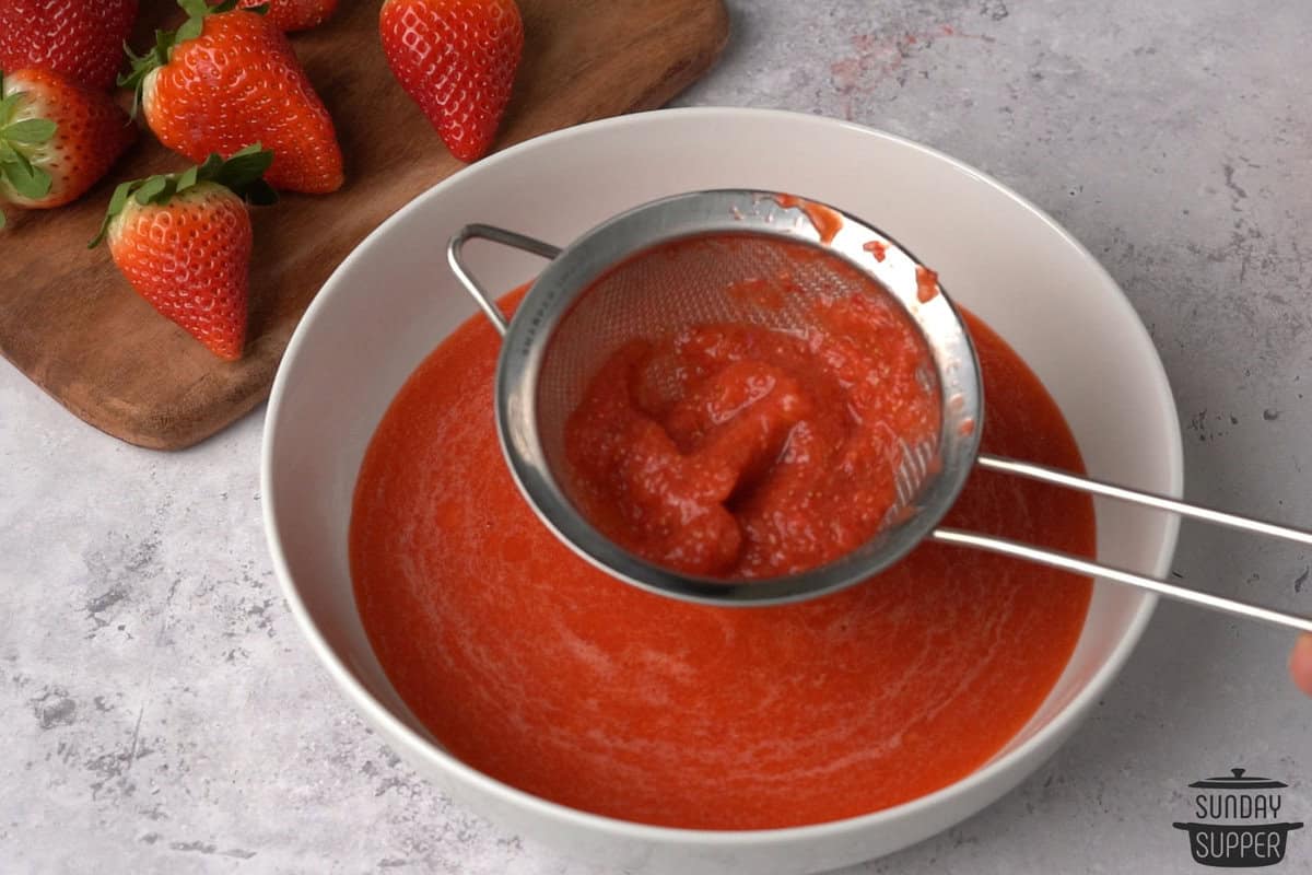 the strawberry puree being passed through a strainer to remove seeds