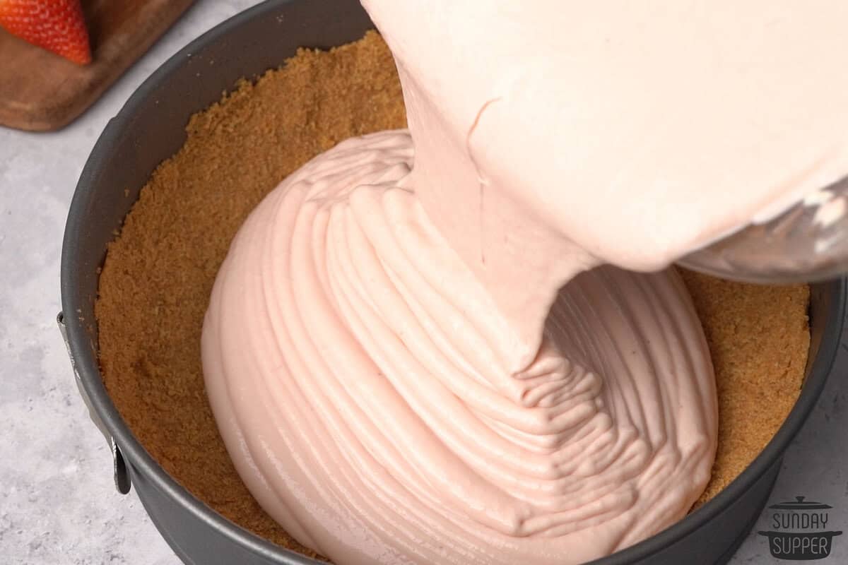 the cheesecake filling being poured into the crust in the pan