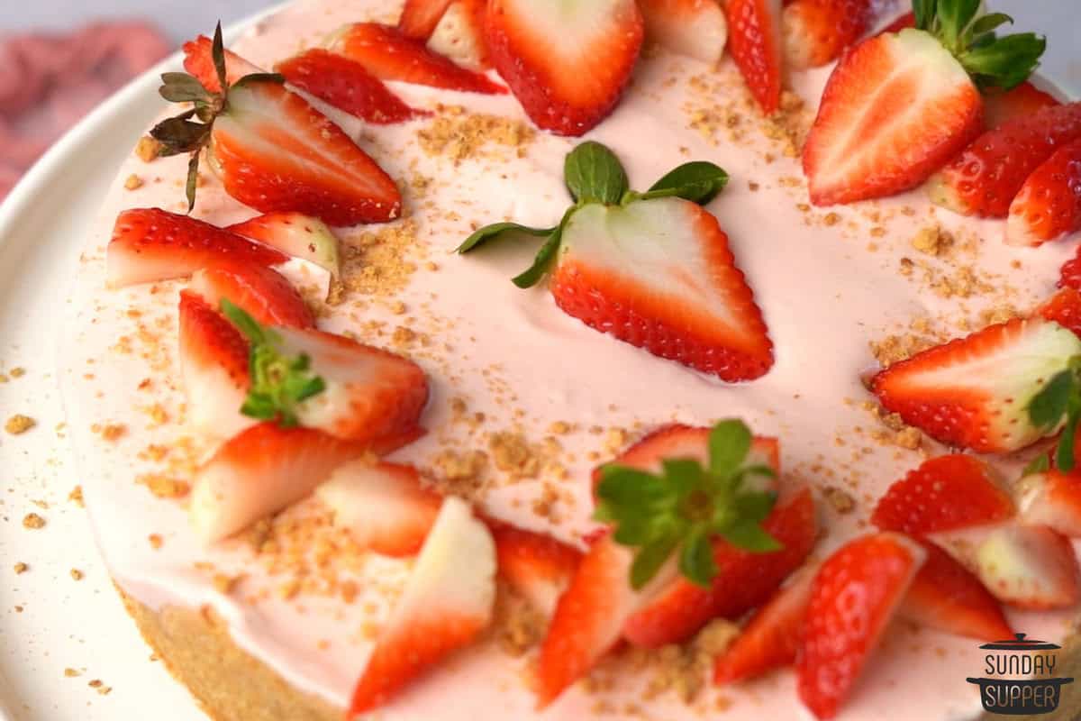 a completed cheesecake after being decorated with graham cracker crumbs and strawberry slices