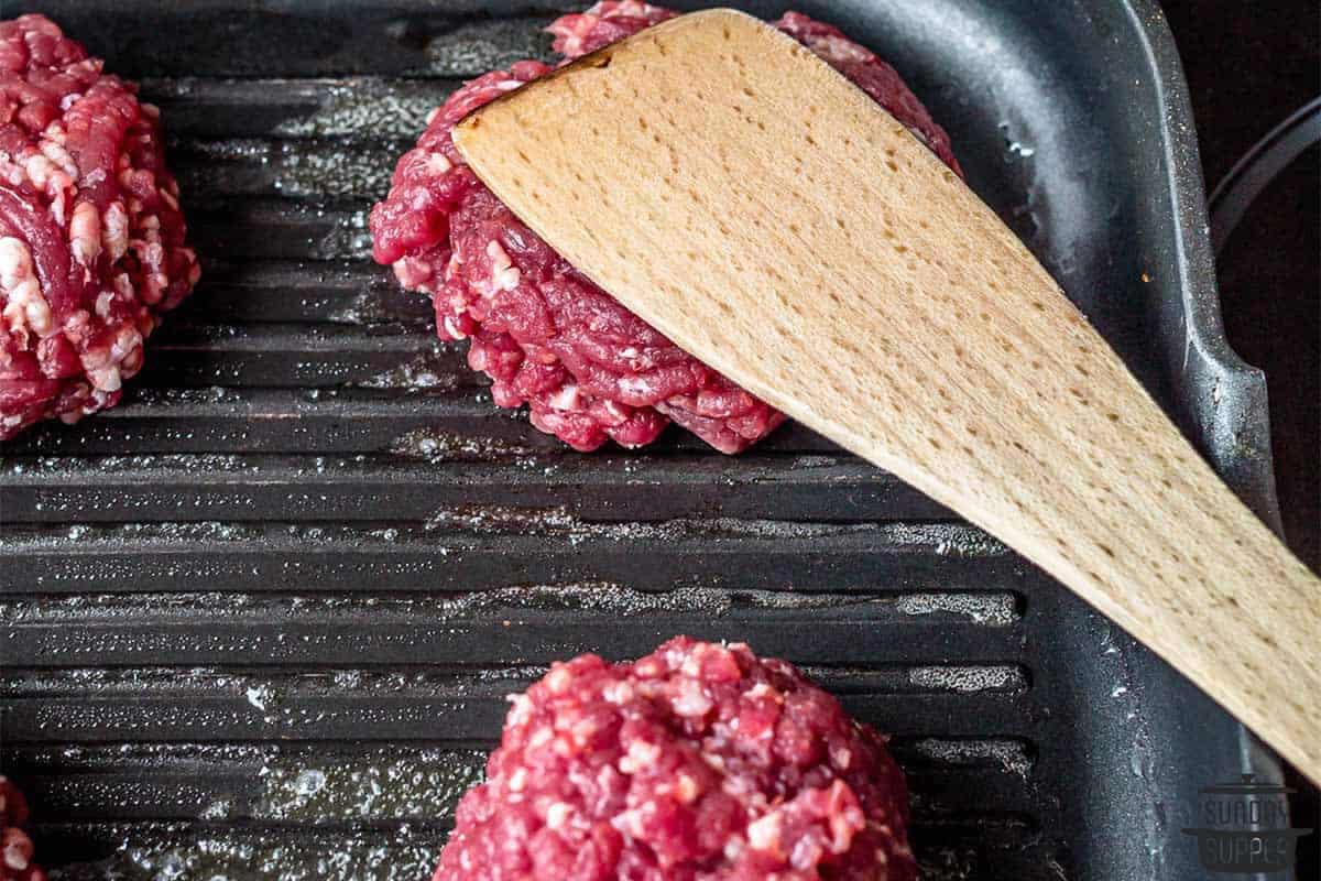 a spatula smashing the burger meat balls flat