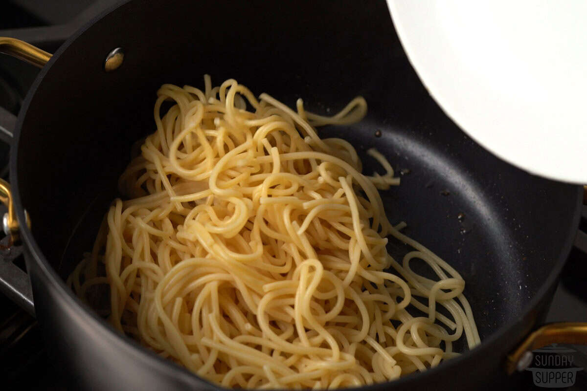 adding cooked noodles to a pot