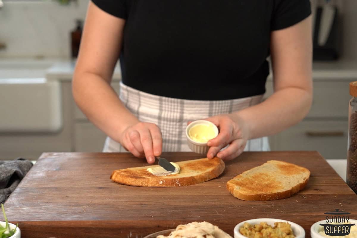 toasted bread being spread with mayonnaise