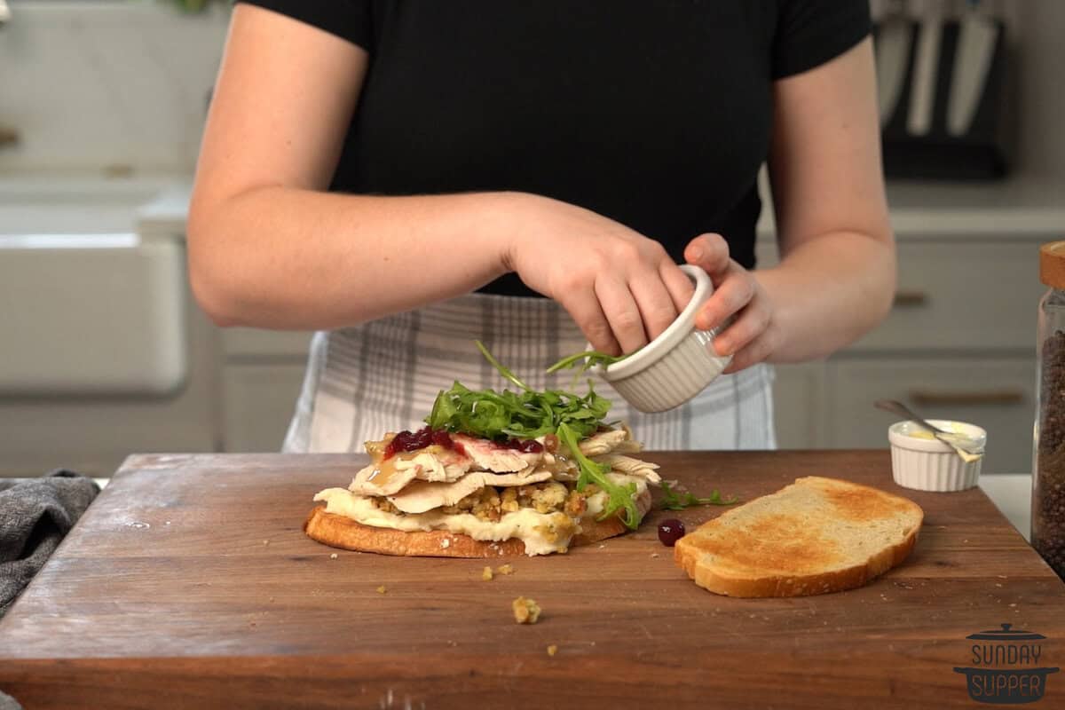 the toppings being layered on the sandwich