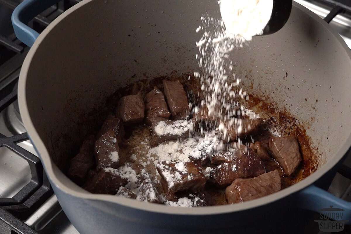 the flour being sprinkled over the browned beef