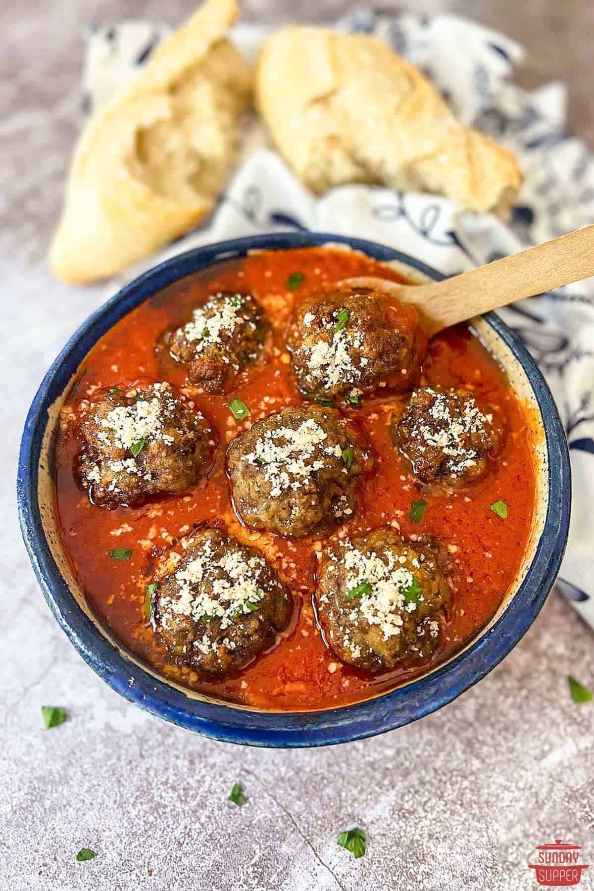 italian meatballs in a bowl with a spoon and french bread