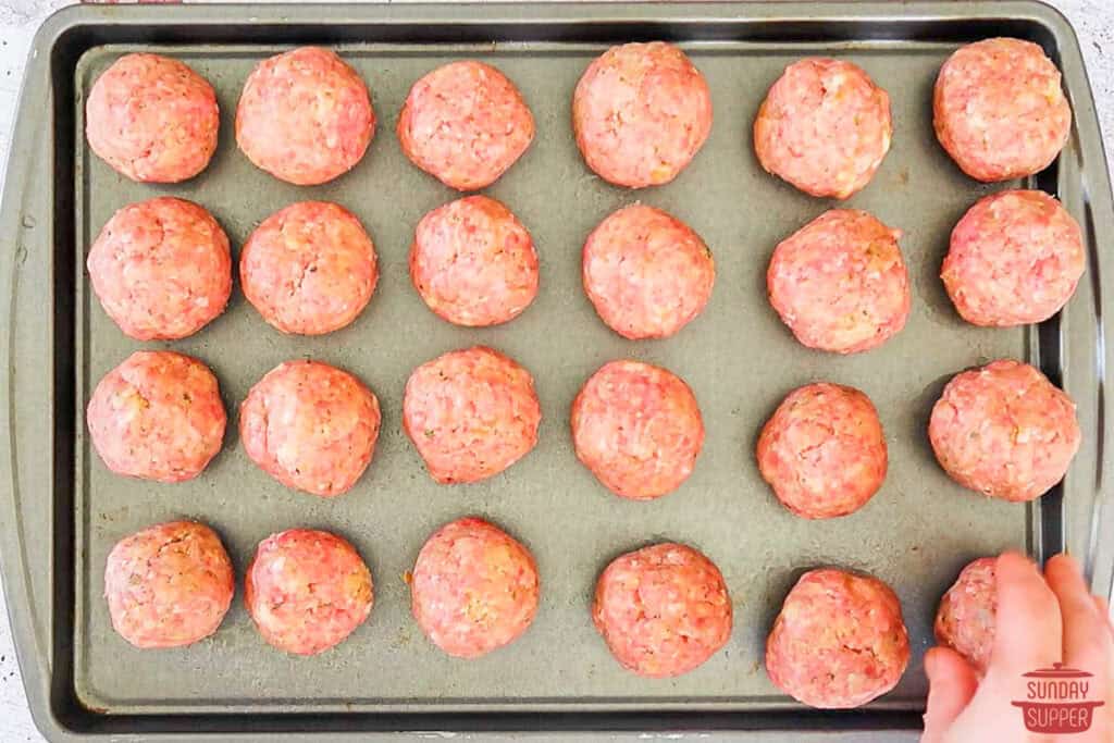 adding rolled meatballs to a baking sheet