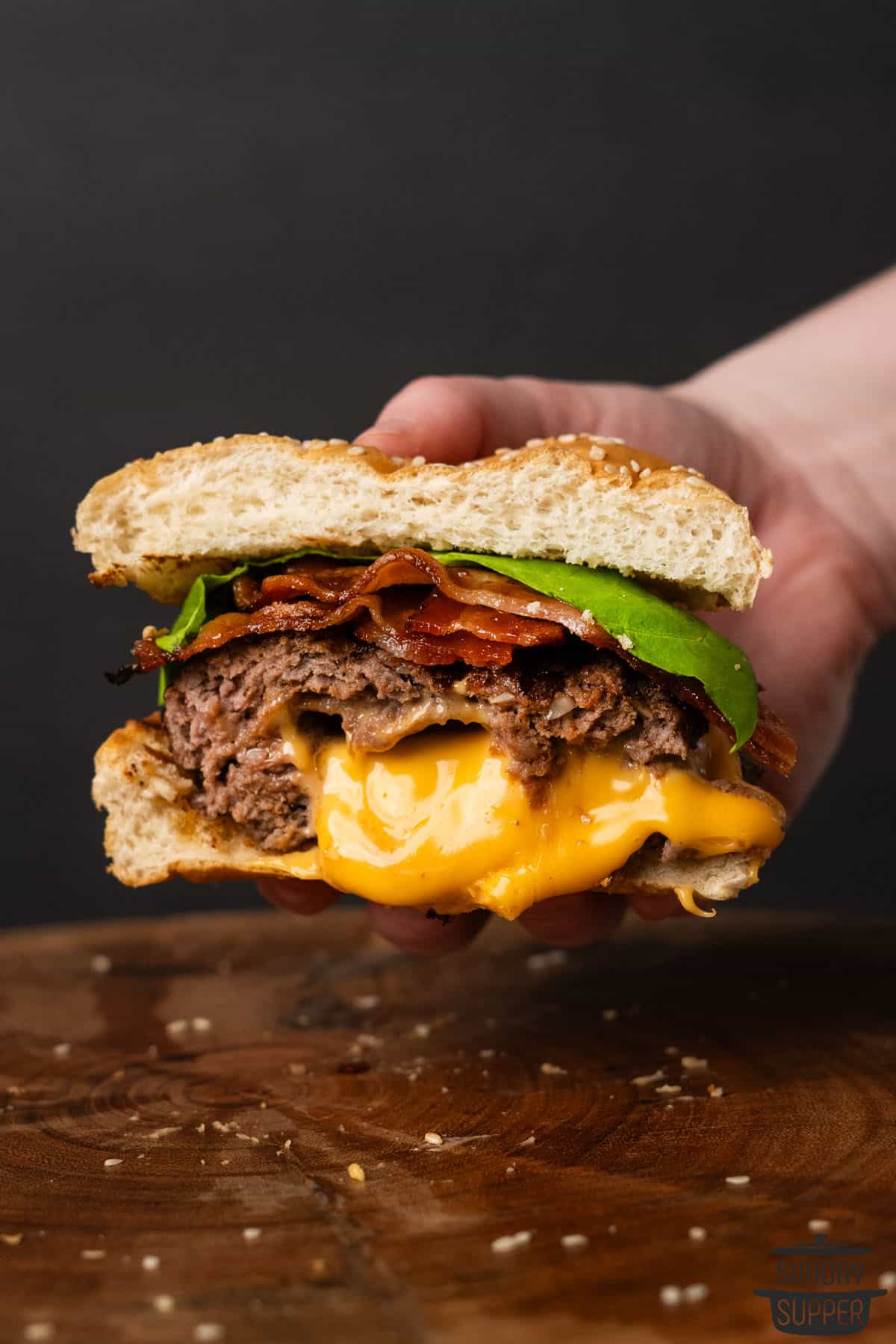 a hand holding a sliced stuffed cheeseburger with melting cheese