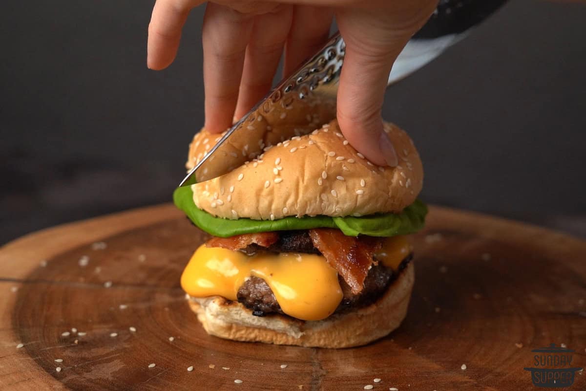 a burger with toppings being sliced open with a knife