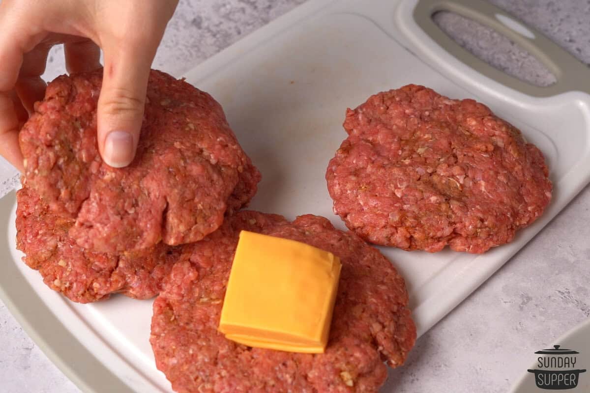 the cheese being added to the patties and another layer of beef being placed on top