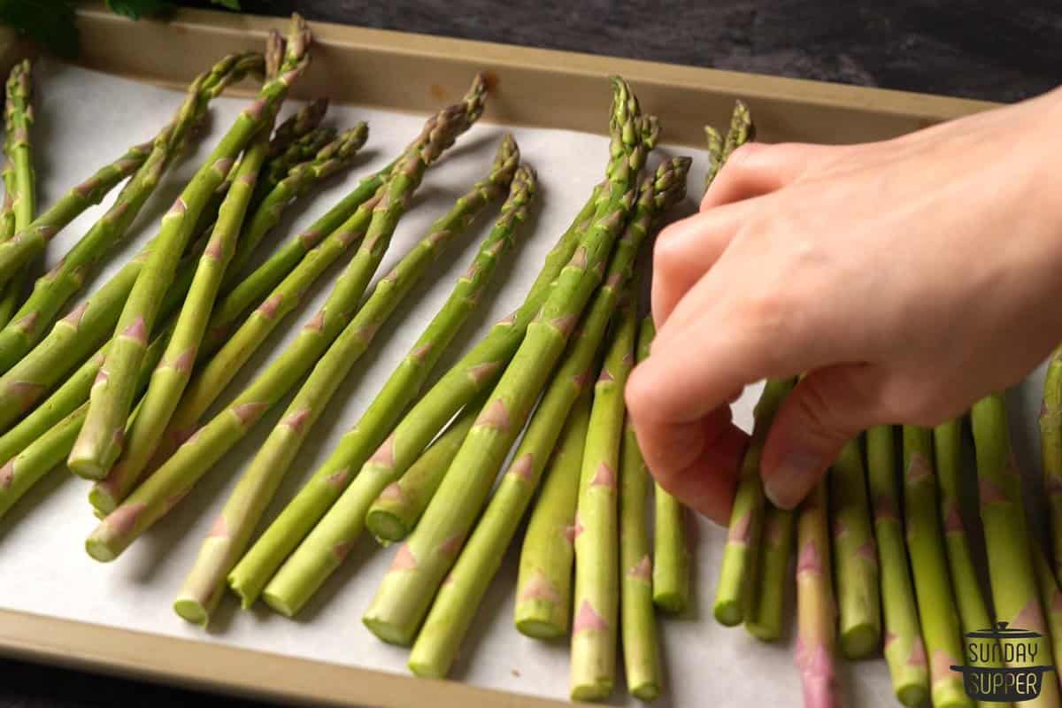 asparagus after being trimmed being placed on a baking dish