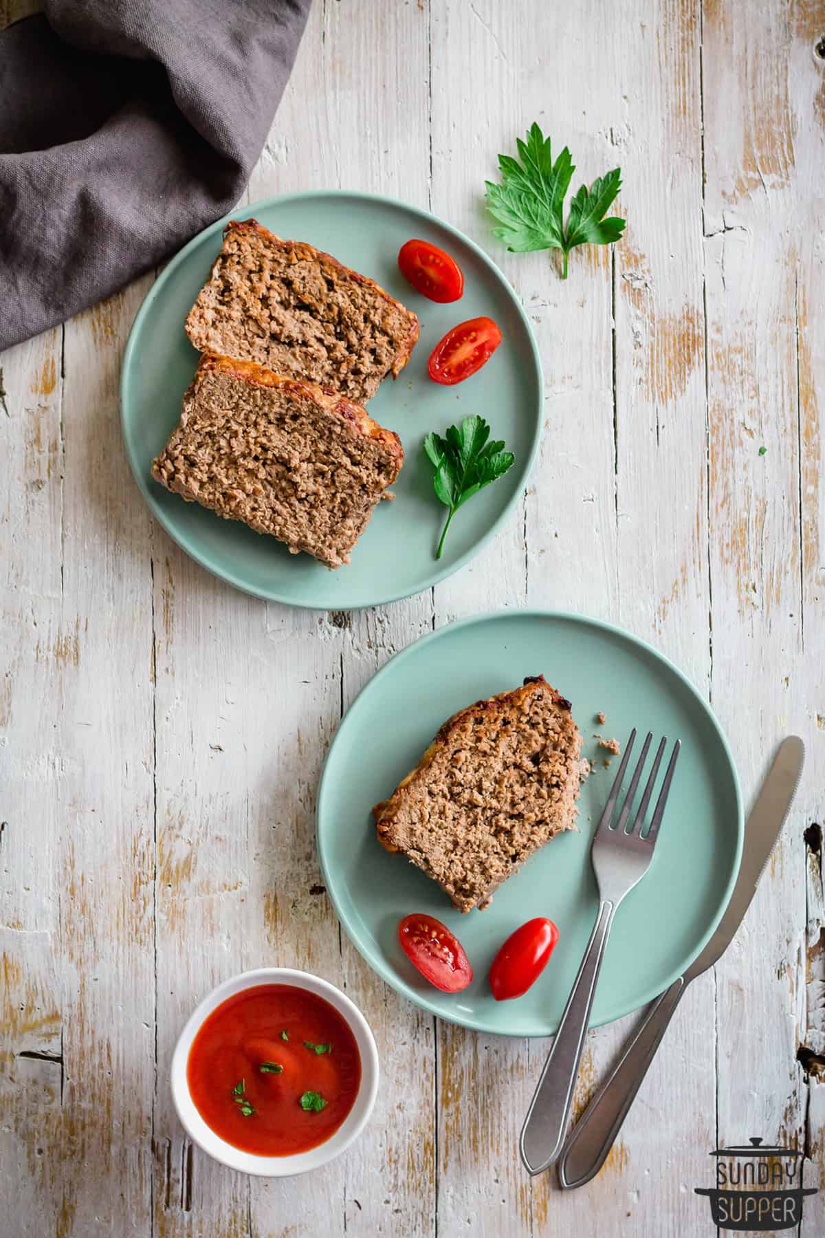 two plates of meatloaf slices with a fork and a knife