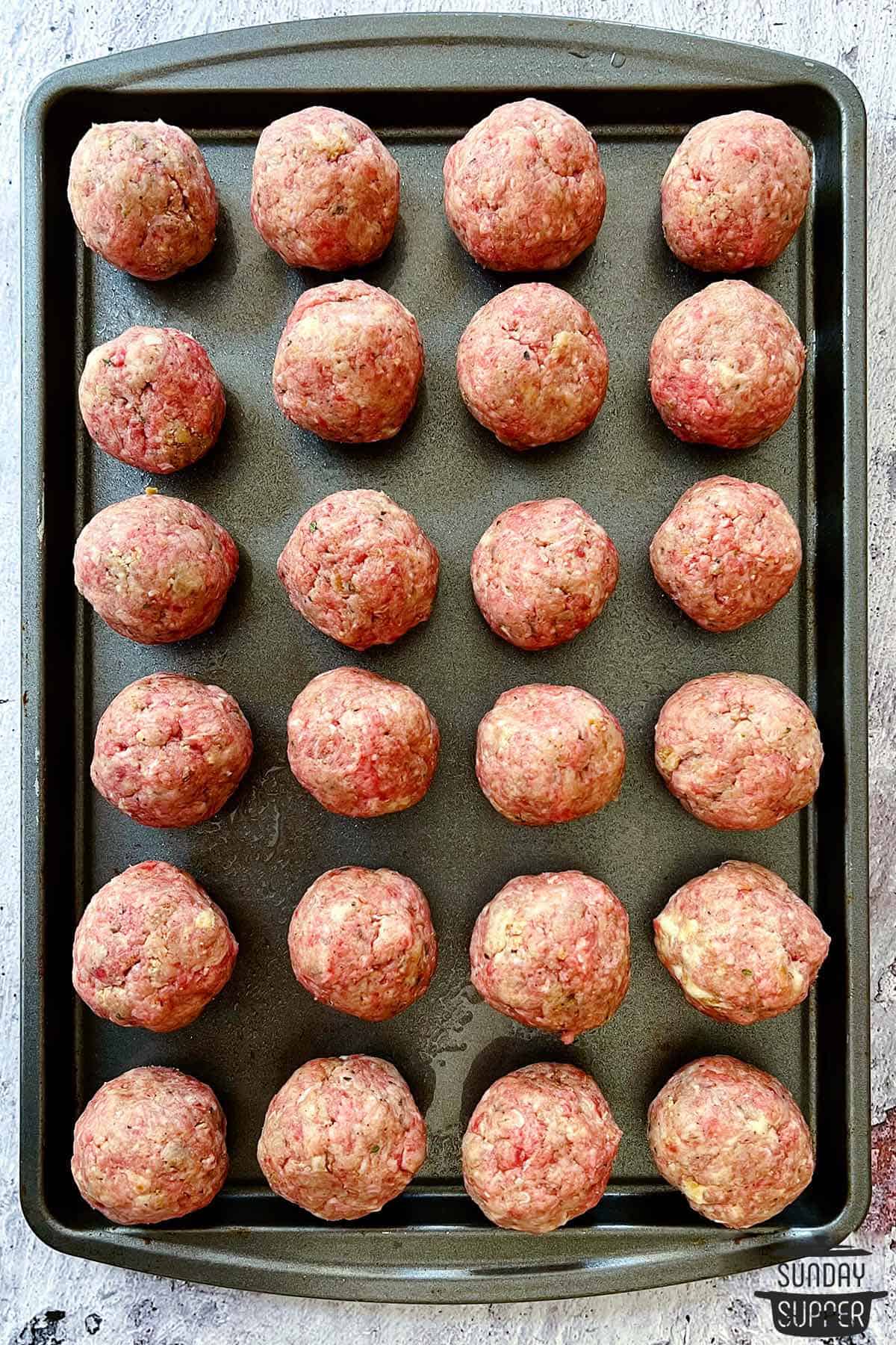 a baking tray with rows of uncooked meatballs ready to bake