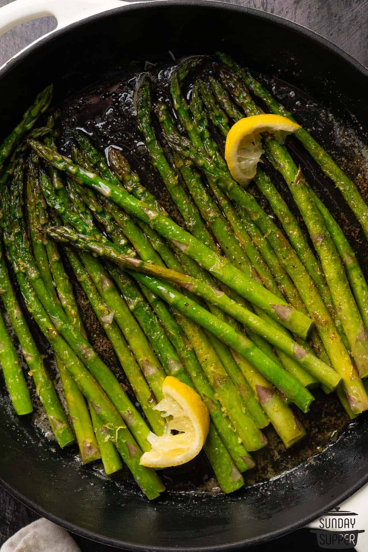 a pan filled with sauteed asparagus and lemon wedges