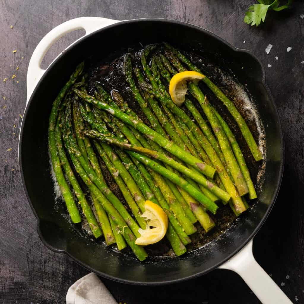 sauteed asparagus in a pan with lemon wedges