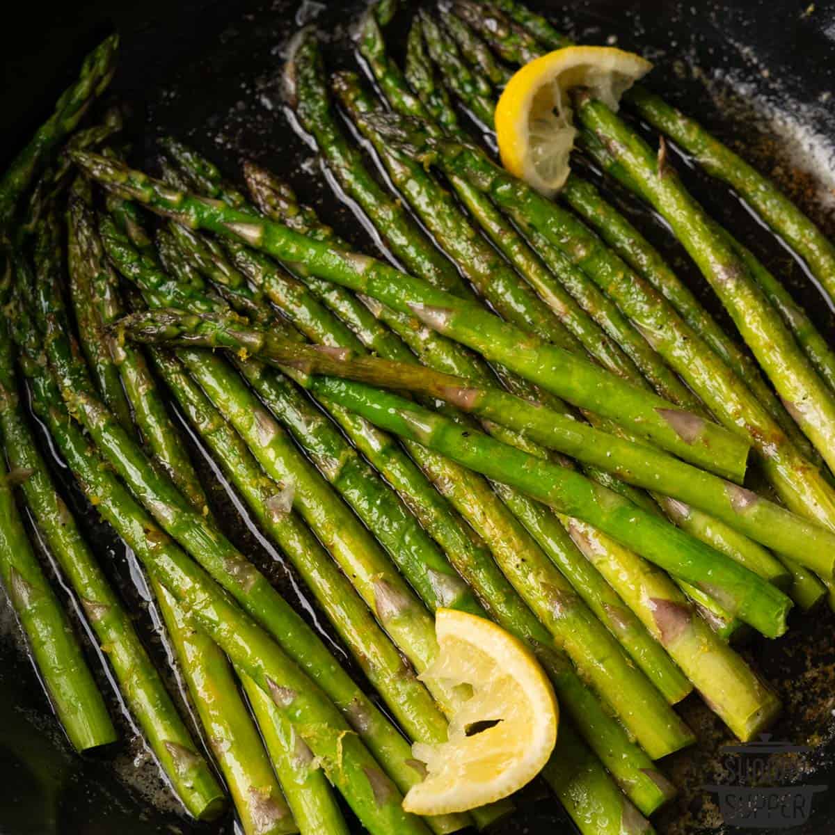 a closeup of lemon wedges and asparagus sauteed in a pan