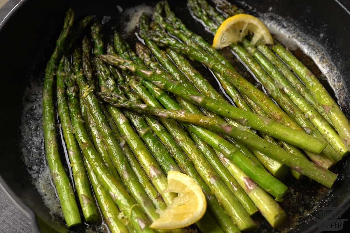 cooked asparagus in a pan with lemon wedges