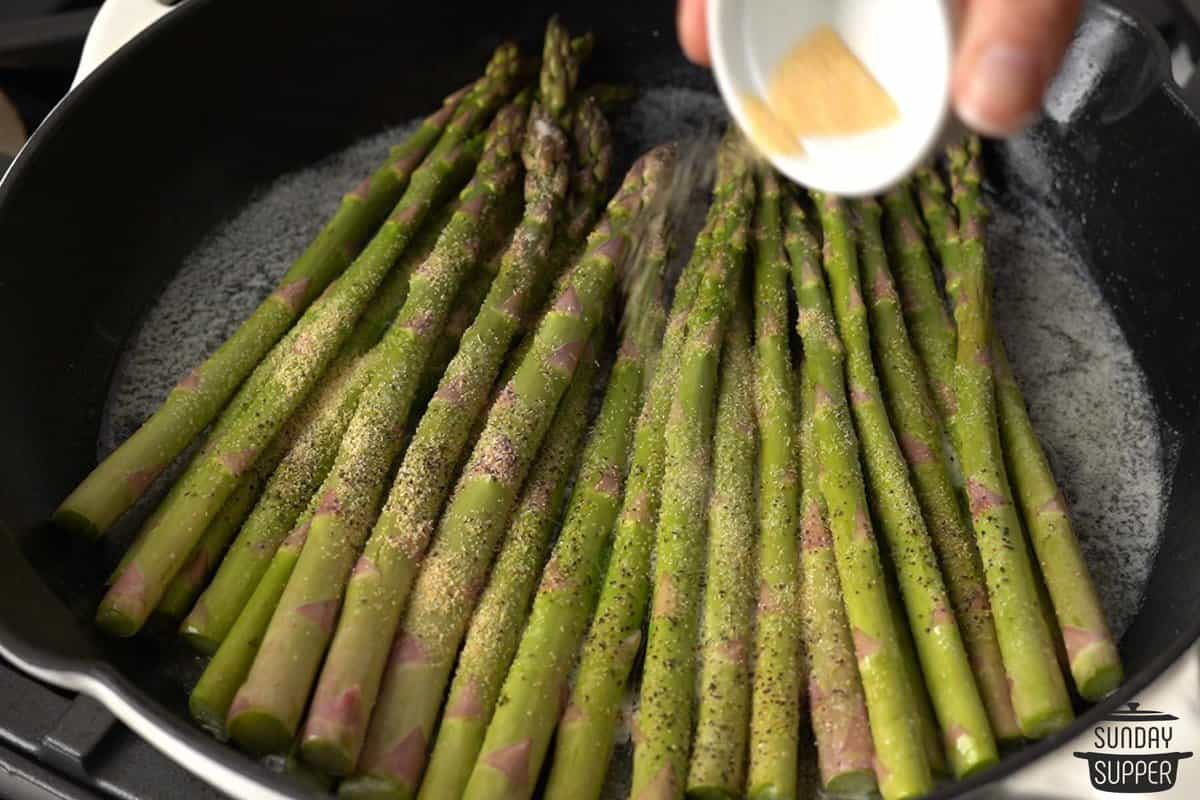 the seasonings being added to the pan of asparagus