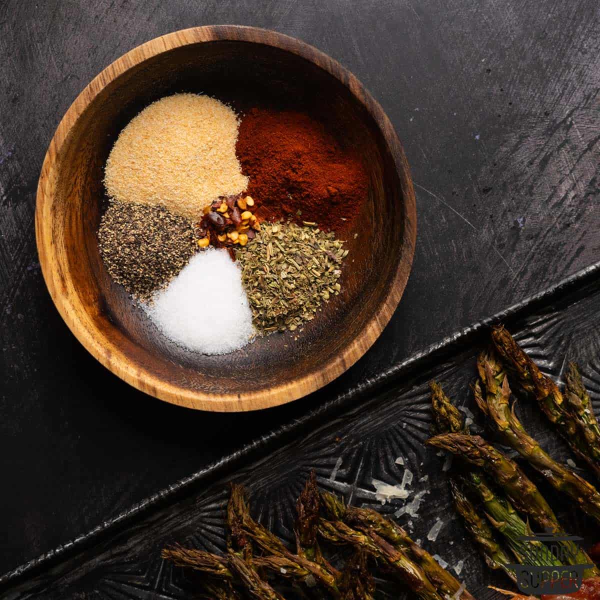 a bowl of seasonings next to asparagus