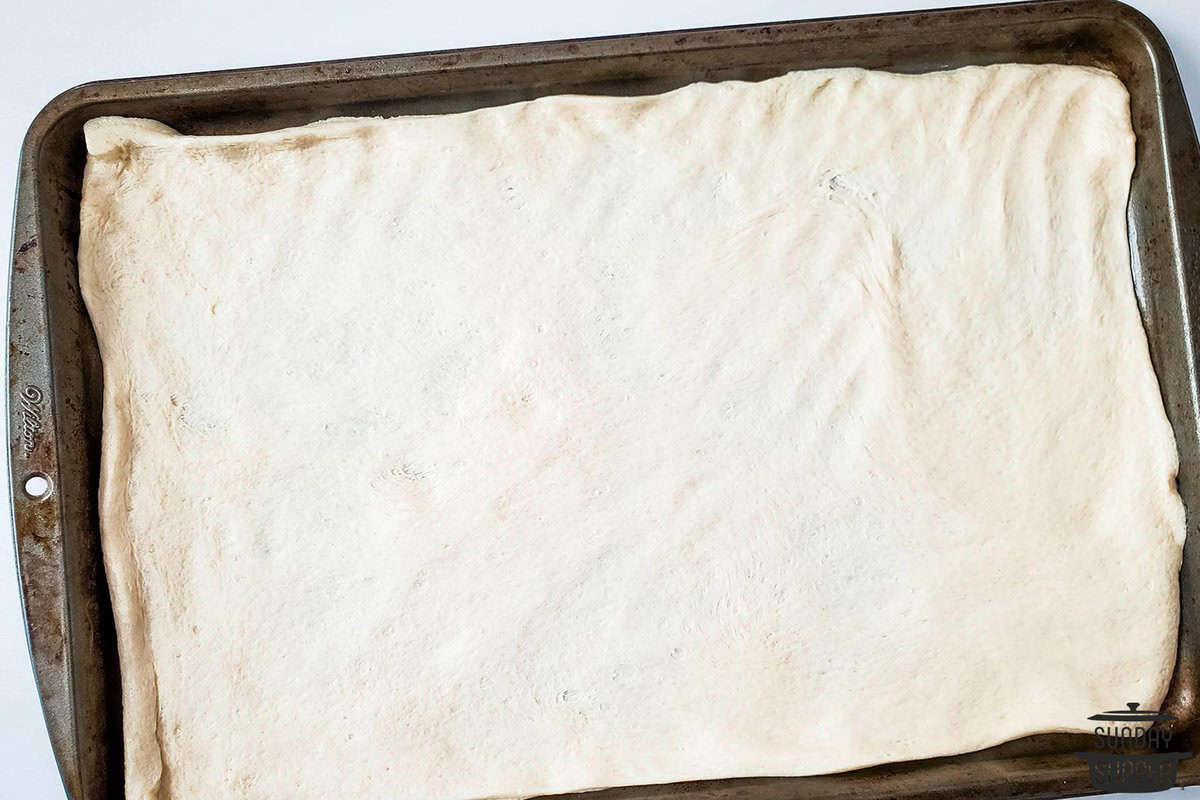 a pizza crust rolled out on a baking sheet