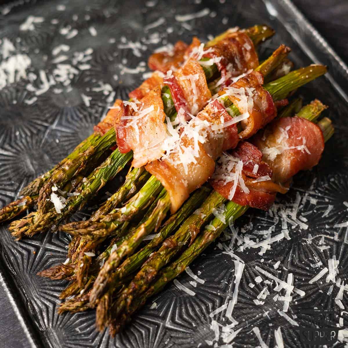 bundles of bacon-wrapped asparagus stacked on a tray