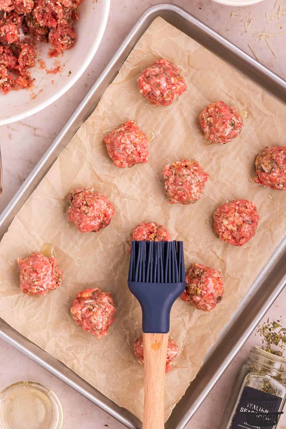 oil being brushed on the meatballs before baking