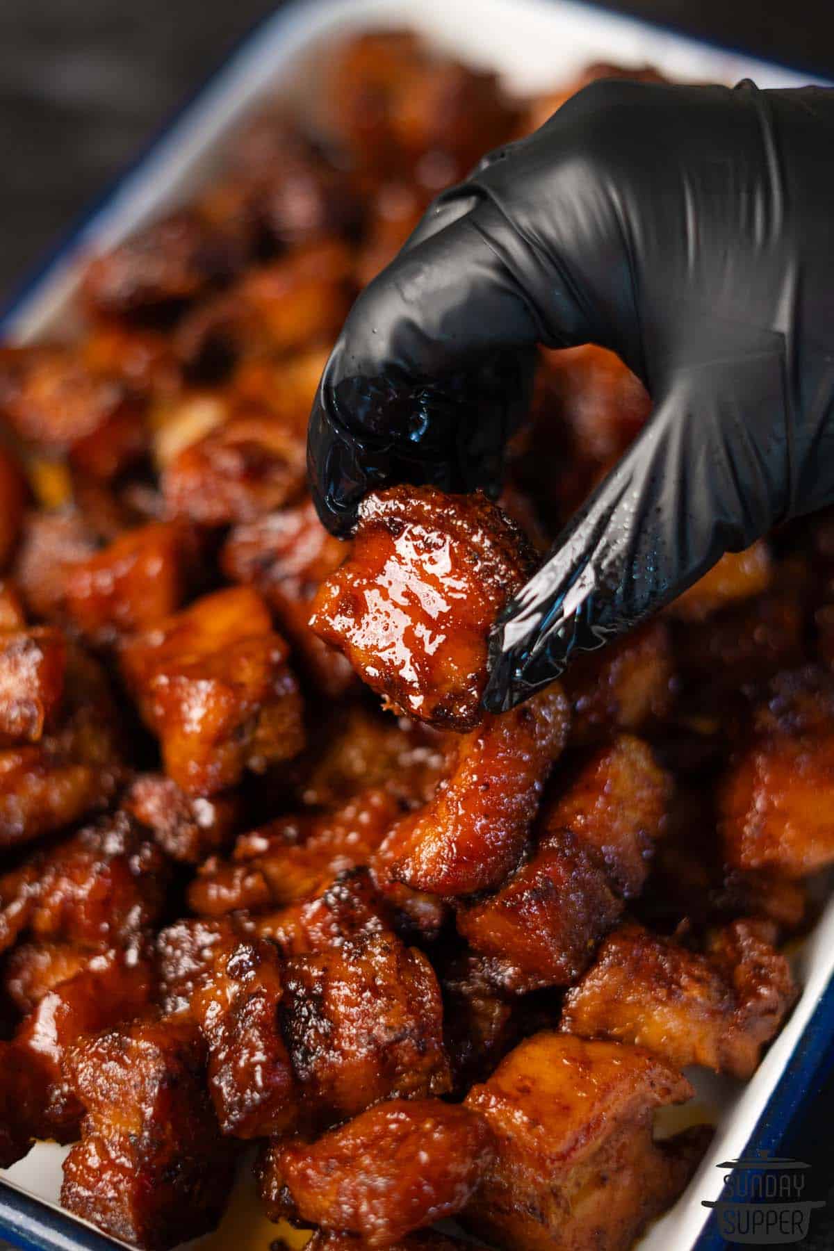 picking up a piece of pork belly burnt ends after cooking in oven