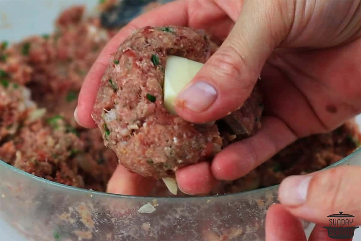 pressing a piece of mozzarella cheese into the meatball