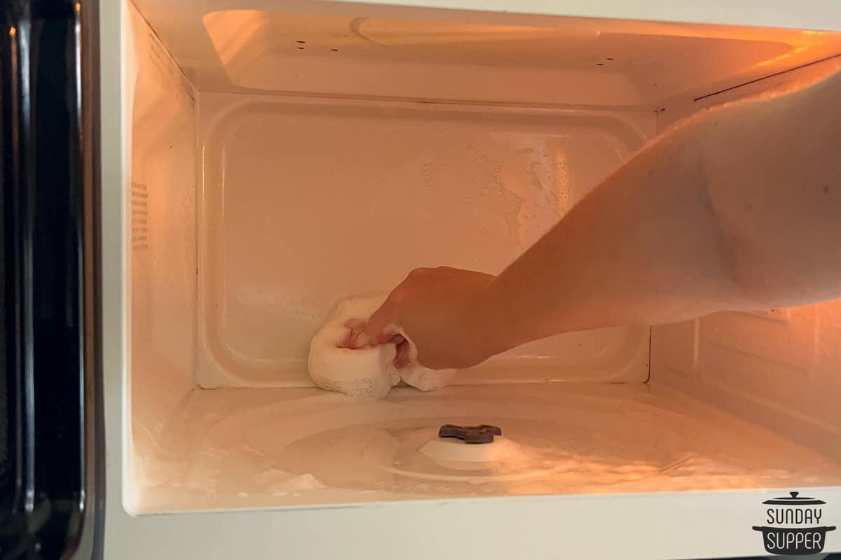 a soapy sponge being used to wipe out the microwave