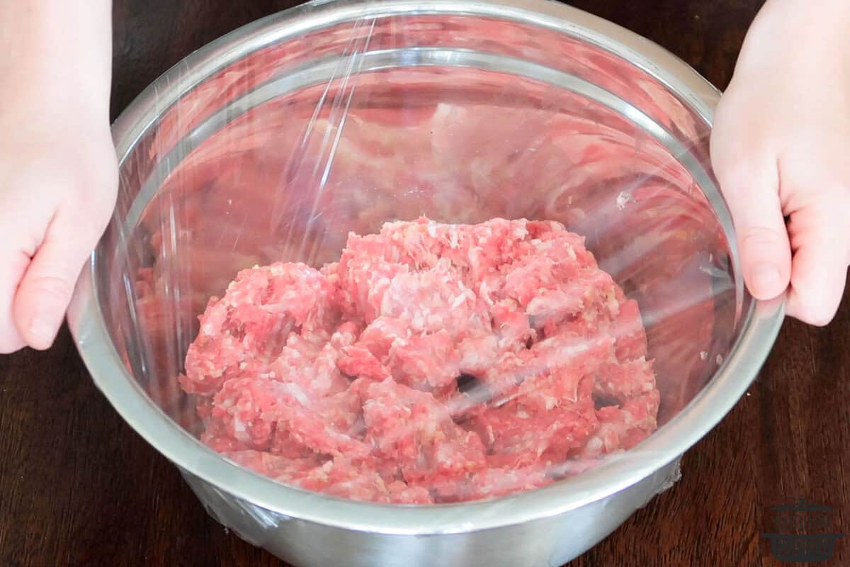 the meatball mixture being covered in plastic to chill