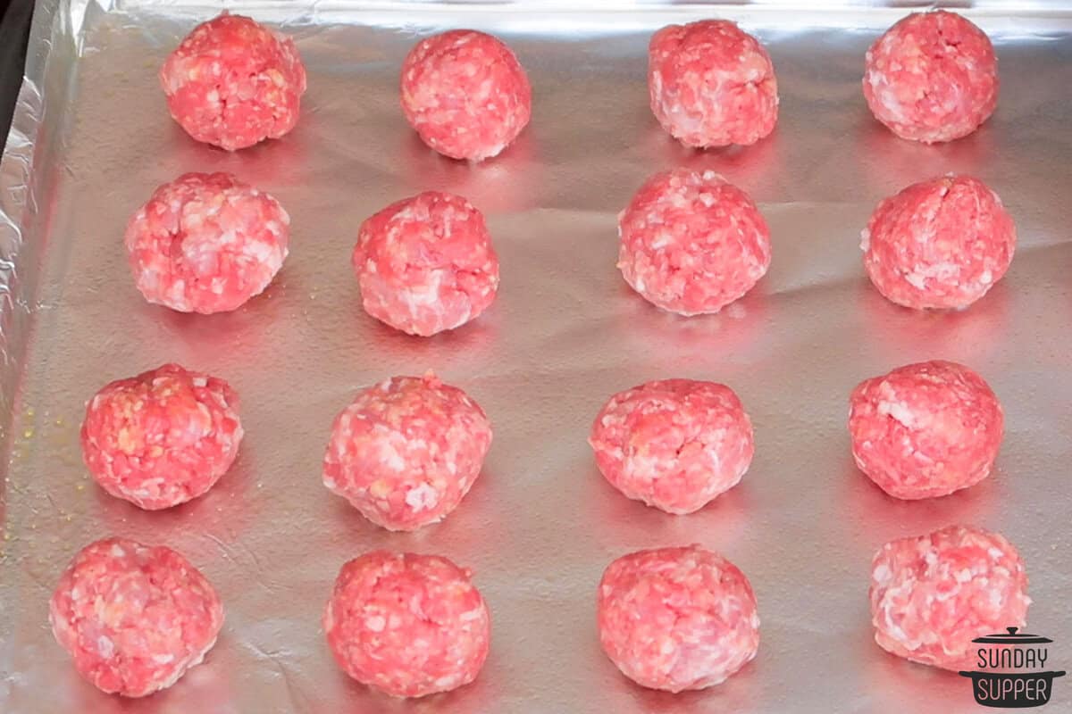 raw meatballs rolled into shape and placed on a baking sheet