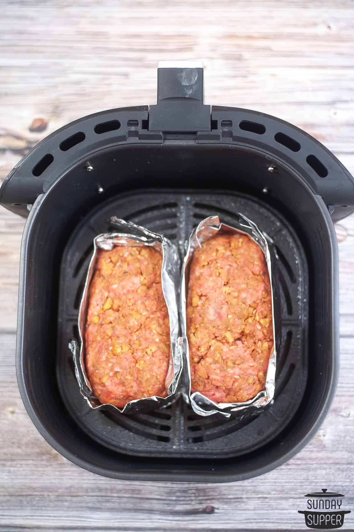 two uncooked meatloaves in an air fryer basket