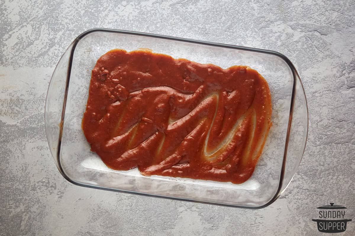 enchilada sauce poured in the bottom of a casserole dish