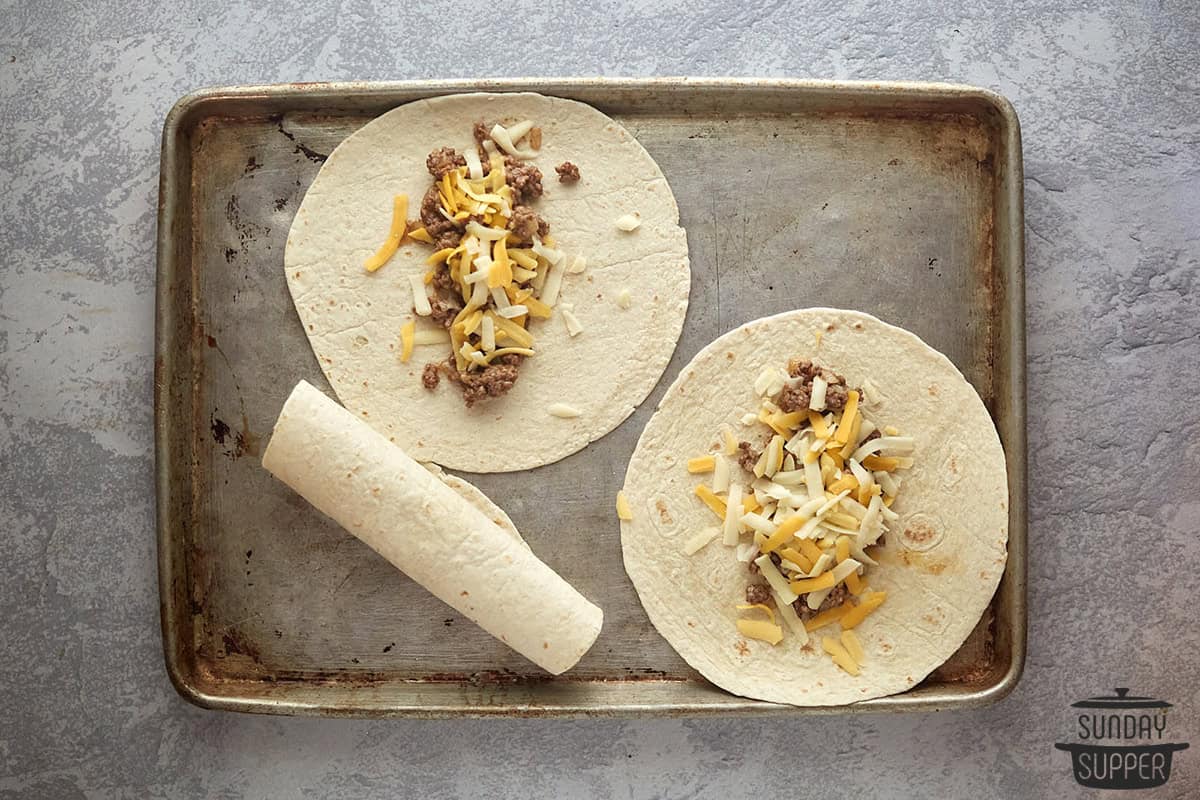 two tortillas on a baking sheet with cheese and beef enchilada fillings