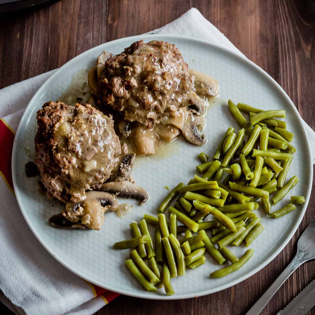 two steaks on a plate with gravy and green beans