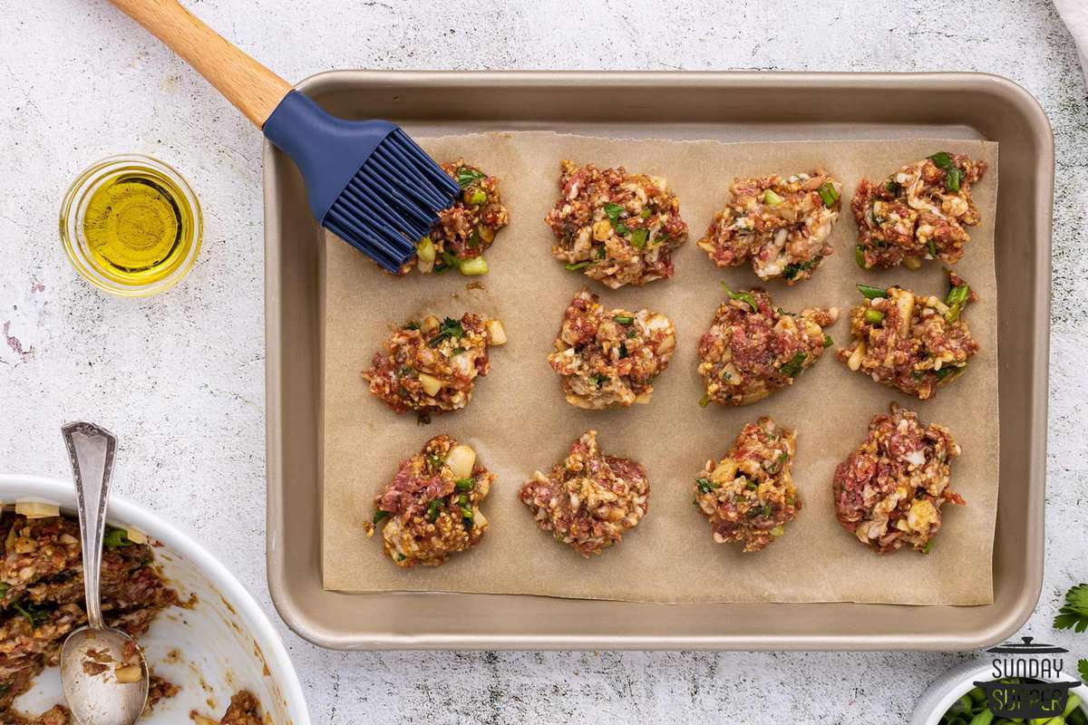 oil being brushed on raw asian meatballs