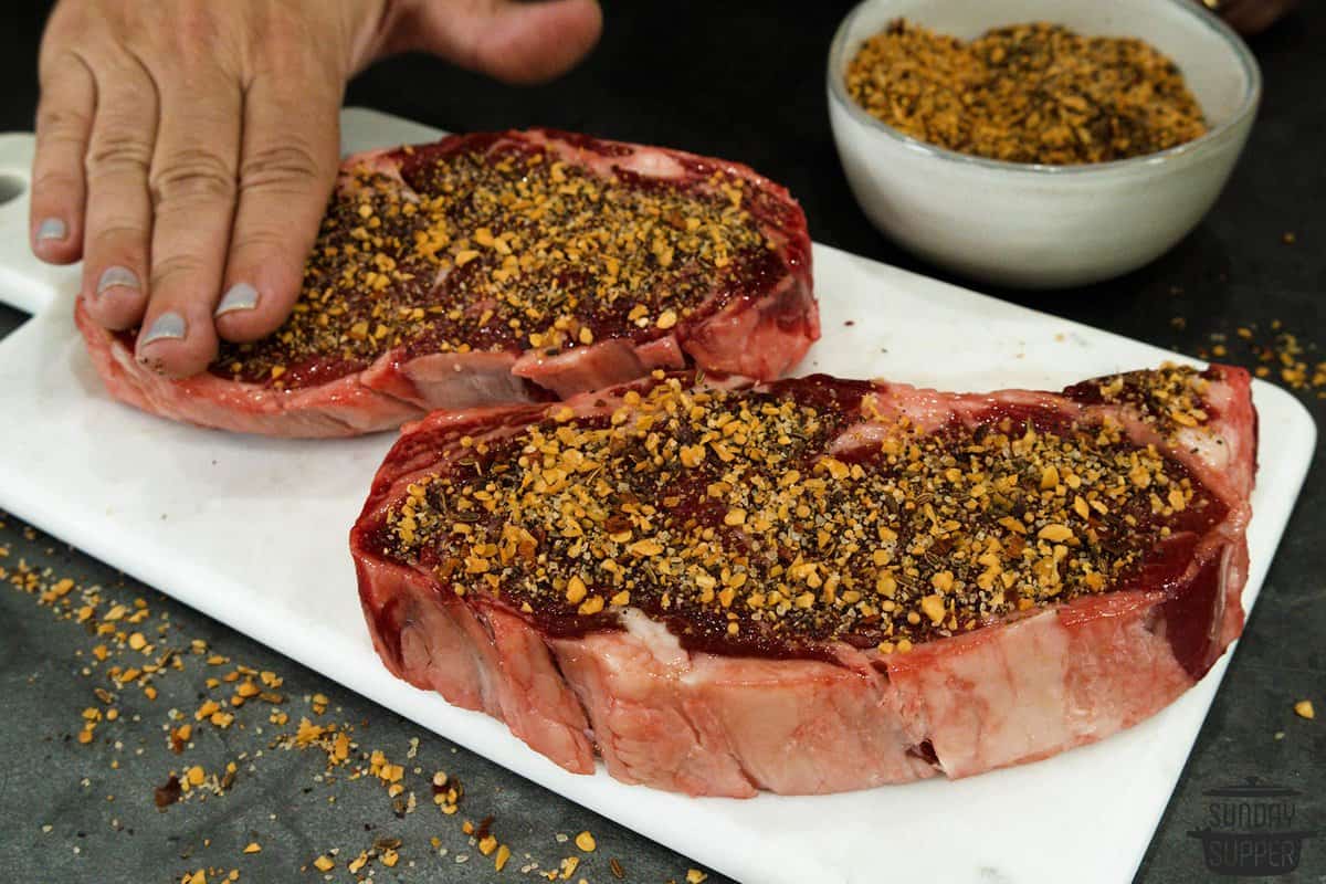 seasonings being patted on to steak