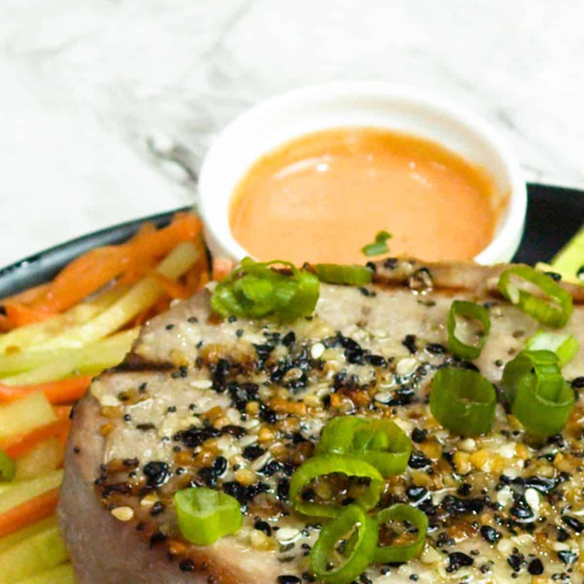 a dipping bowl of sriracha mayo with a grilled tuna steak and vegetables