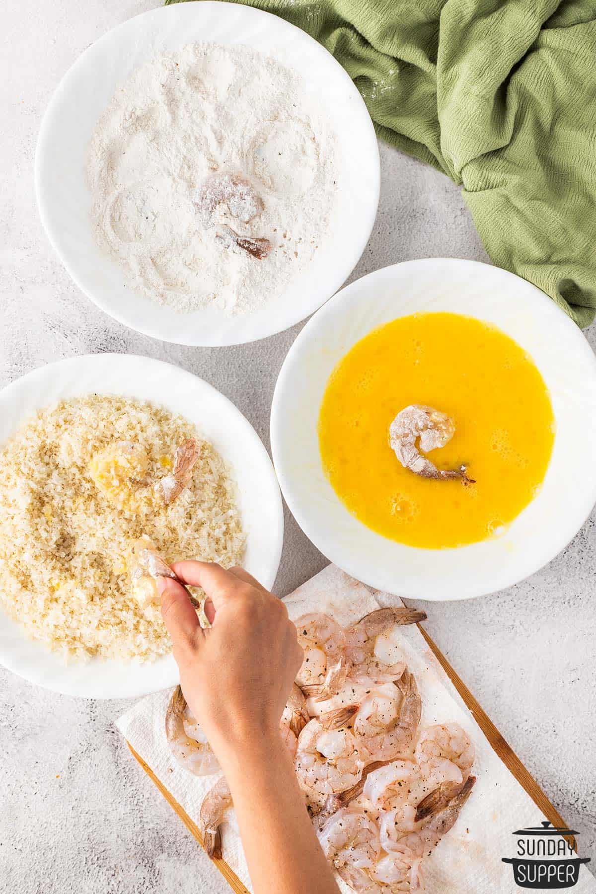 the shrimp being breaded by using three bowls of breading materials