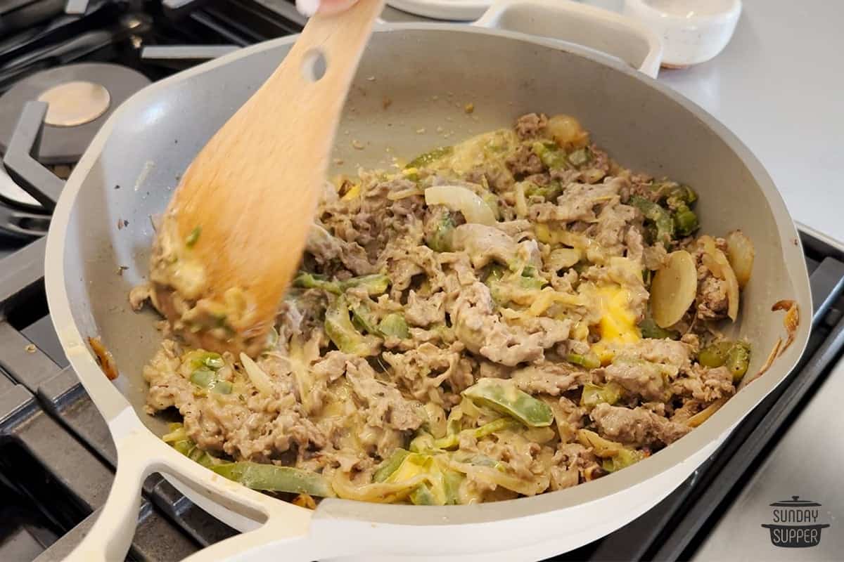 stirring shredded steak with peppers and onions in pan