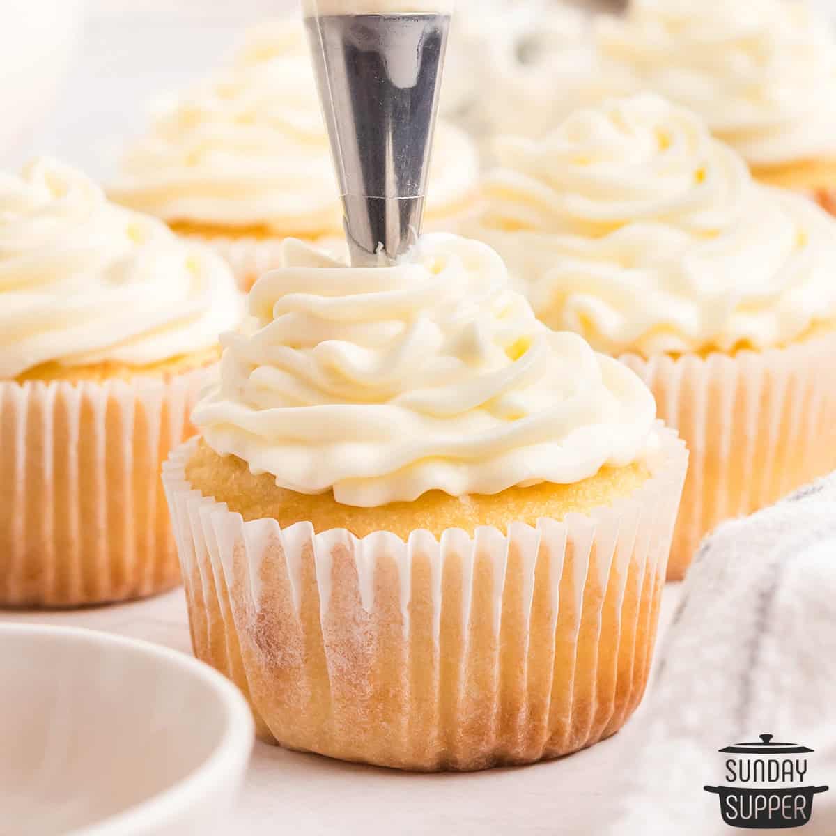 cream cheese frosting being piped on to a cupcake