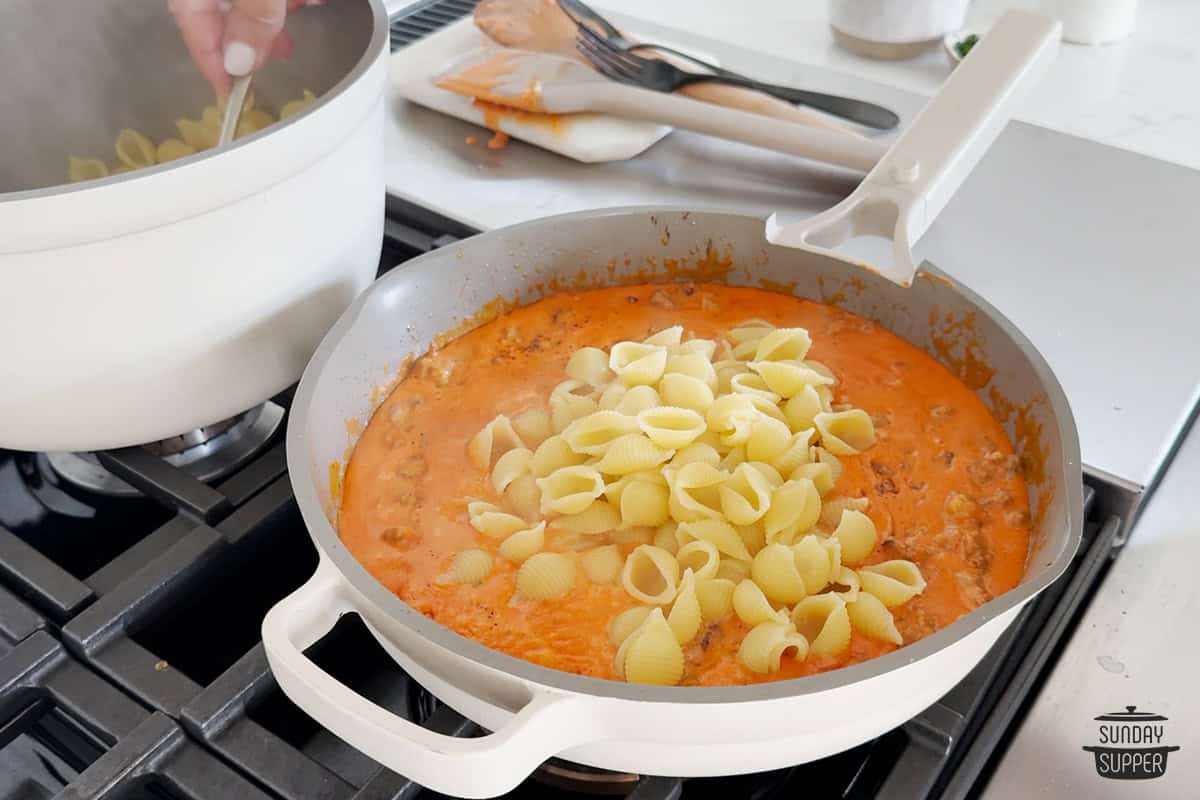 adding pasta to pink pasta sauce