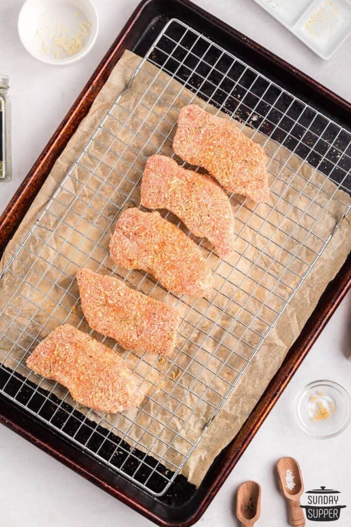 coated pork chops on rack on baking sheet