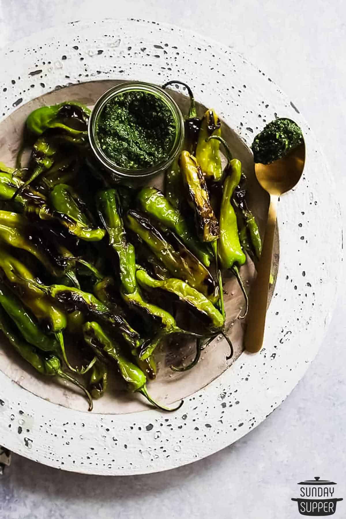 blistered shishito peppers on a plate with a cup of pesto