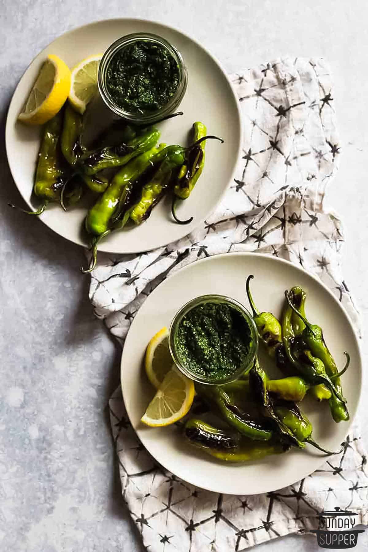 two plates of shishito peppers with pesto and lemon wedges