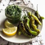 a plate with lemon wedges, pesto, and blistered shishito peppers