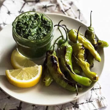 a plate with lemon wedges, pesto, and blistered shishito peppers