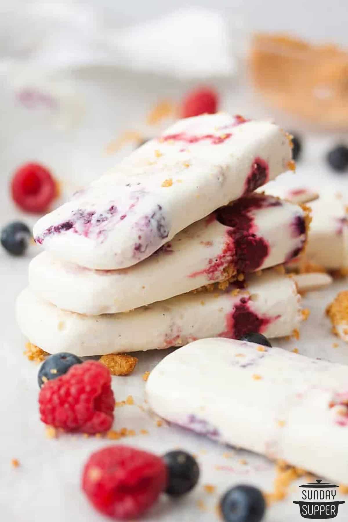 a pile of three cheesecake popsicles with extra berries